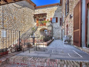 A stone courtyard with outdoor seating, a staircase, and a view of a building with wooden shutters. - La Corte di Muciafora (Muciafora)
