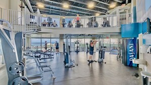 A multi-level gym with various exercise equipment, a view of the ocean, and a blue wall with the word "PASANI". - Bright & Spacious Condo 1BD! Steps from the Beach! (Panama City Beach)