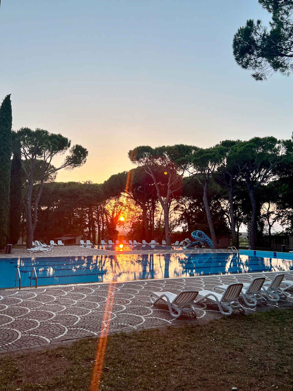 A swimming pool with lounge chairs and a sunset in the background.