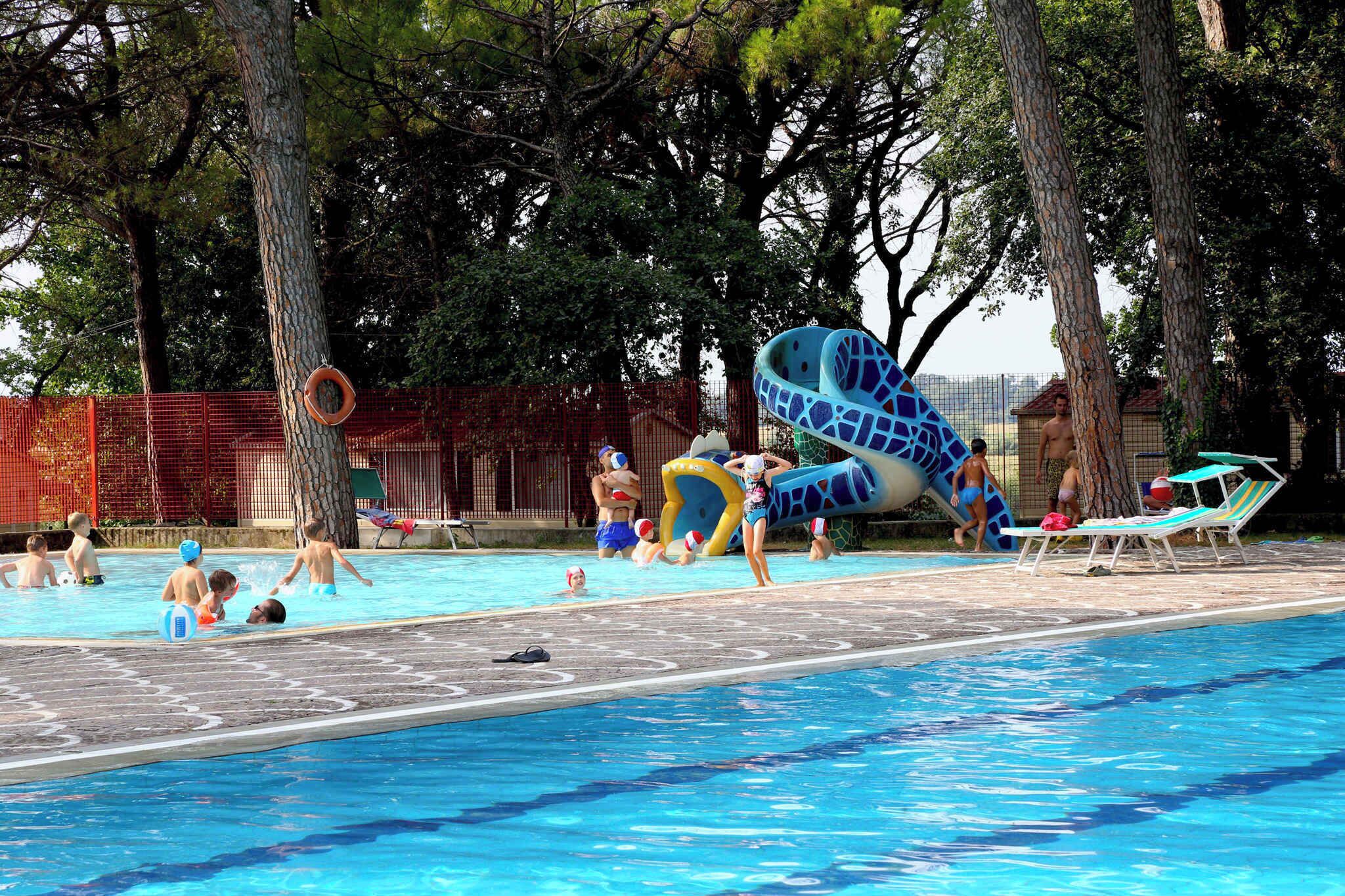 Una piscina con tobogán, árboles y sillas de descanso.