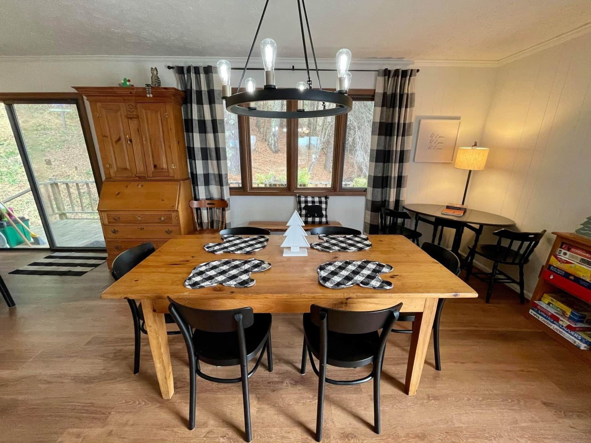 A dining area with a wooden table, black chairs, a chandelier, and checkered placemats.