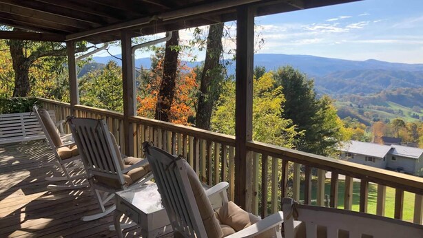 A covered deck with wooden chairs and a table, overlooking a scenic view of mountains and trees. - Delightfully rustic 4-bedroom house in Vilas with stunning long-range views. (Vilas)
