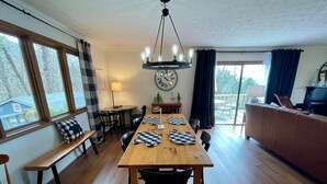 A dining area with a wooden table, black chairs, a chandelier, and a view of the outdoors through large windows. - Delightfully rustic 4-bedroom house in Vilas with stunning long-range views. (Vilas)