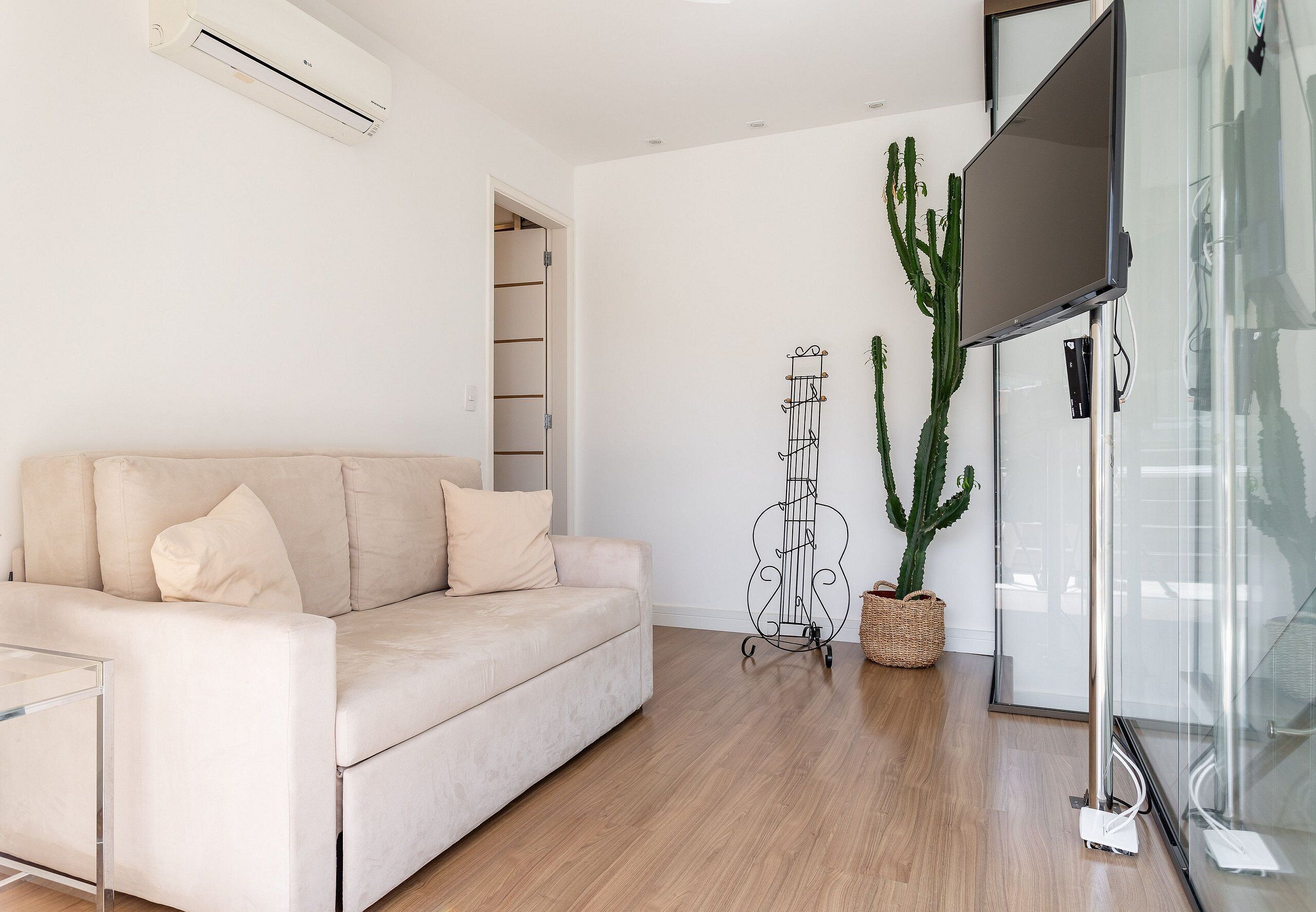 Un salon moderne avec un canapé beige, une table basse en verre, une plante succulente et un téléviseur fixé au mur.