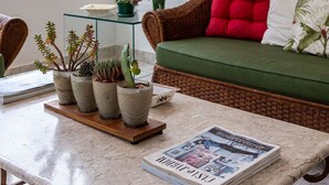 En hyggelig stue med en grøn sofa, et sofabord med planter, og grønne omgivelser udenfor.