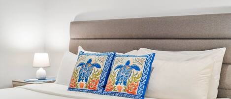 Een keurig opgemaakt bed met twee decoratieve kussens, een bedlampje en een wand met ingelijste kunstwerken.