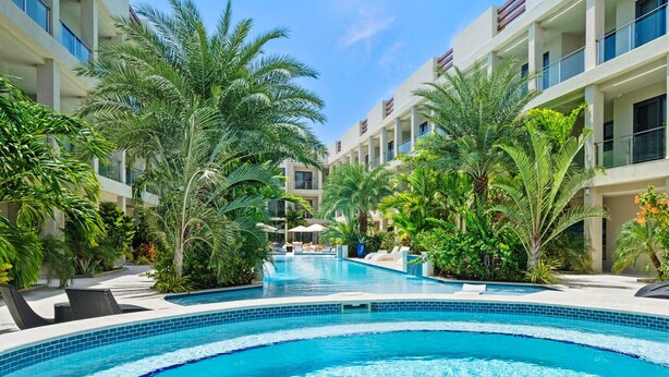 A swimming pool surrounded by lush greenery and modern buildings. - Wariruri Condos by SunStays (Noord)