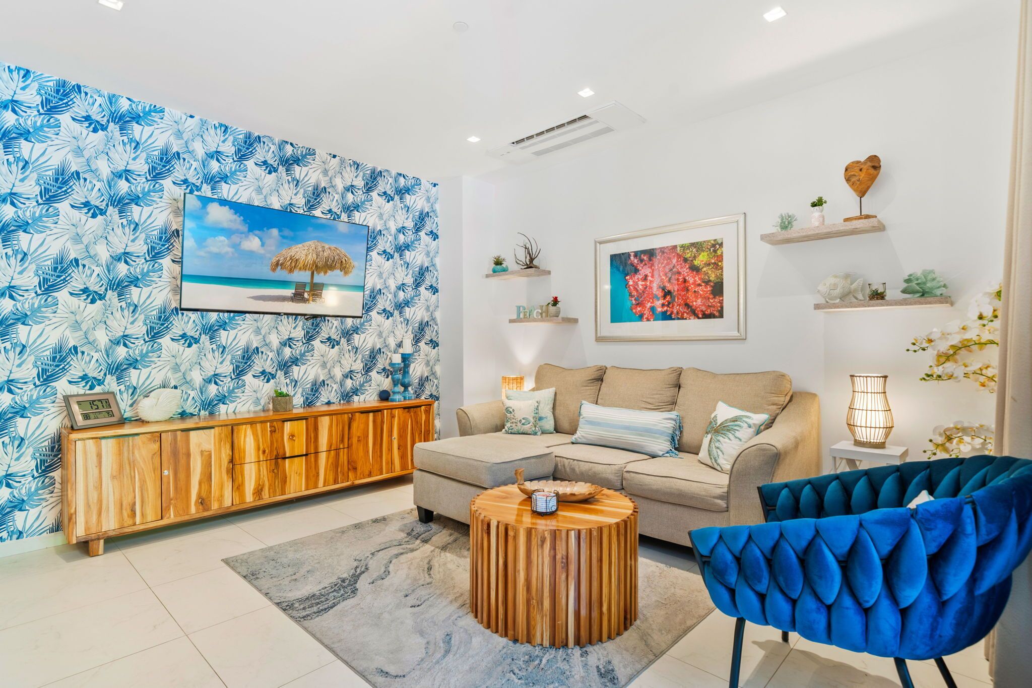 Ein modernes Wohnzimmer mit einer Couch, einem blauen Sessel, einem Holztisch und Tapete mit tropischen Blättern.