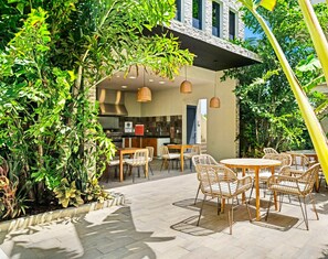 Een terras buiten met een eethoek, inclusief rieten stoelen en een tafel, omringd door weelderige begroeiing.