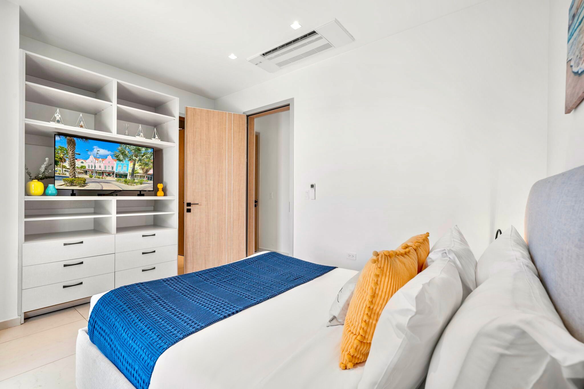 A modern bedroom with a bed, a wardrobe, and a television displaying a scenic view.