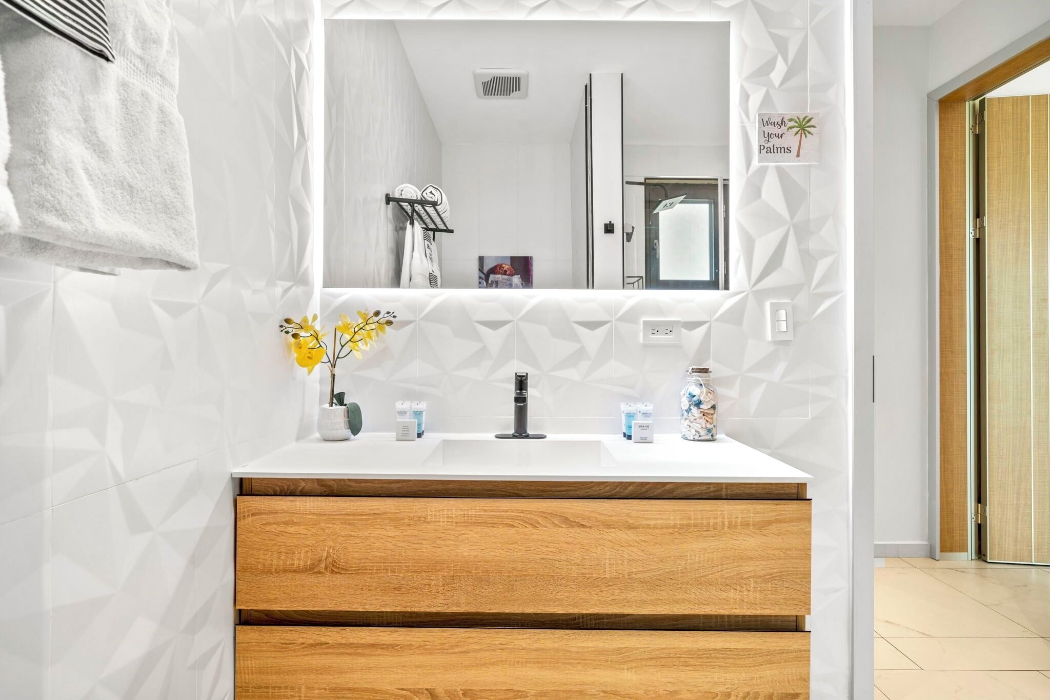 Ein Badezimmer mit einem weißen Waschtisch, Holoszieren, einem Spiegel und einem Handtuch an der Wand.