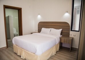 A neatly arranged bedroom with a wooden headboard, a bed with white bedding, a bedside table, and a mirror.