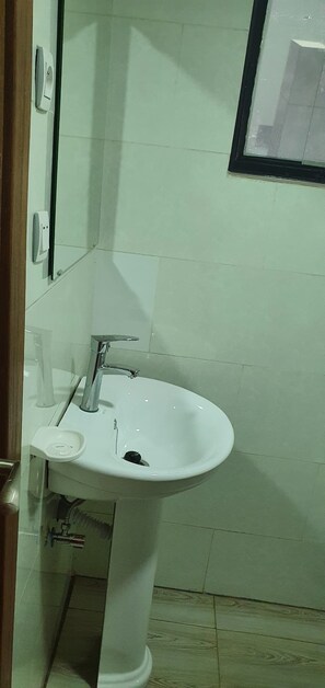 A bathroom with a white pedestal sink, a mirror, and a soap dispenser.