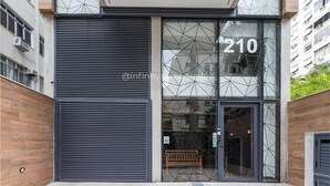 A modern building entrance with a large glass door, number 210, and a wooden bench outside.
