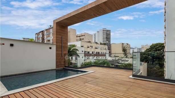 A rooftop pool area with a wooden deck and a clear view of surrounding buildings.