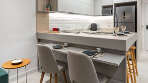 Une cuisine moderne dotée d’un îlot central, de deux tabourets de bar, d’une petite table ronde et d’un micro-ondes encastré.