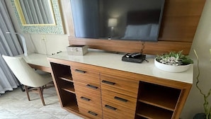 A modern living room with a large flat-screen TV mounted on the wall, a wooden entertainment unit with drawers, a small table with a remote control, and a potted plant. - 3-bedroom condo in enchanting Sint Maarten (Sint Maarten)