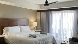 A hotel room with a large bed, a ceiling fan, a bedside table with a lamp, a window with sheer curtains, and a potted plant. - 3-bedroom condo in enchanting Sint Maarten (Sint Maarten)