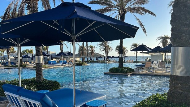 A poolside area with lounge chairs and umbrellas, palm trees, and a clear view of the sea. - 3-bedroom condo in enchanting Sint Maarten (Sint Maarten)