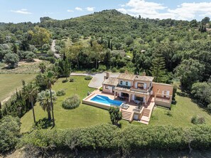 A Mediterranean-style villa with a swimming pool, surrounded by lush greenery and hills.