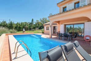 A swimming pool with lounge chairs, a patio with a table and chairs, and a building with a tiled roof and windows. - Villa Zahara - paceful retreat in the countryside (Alcúdia)