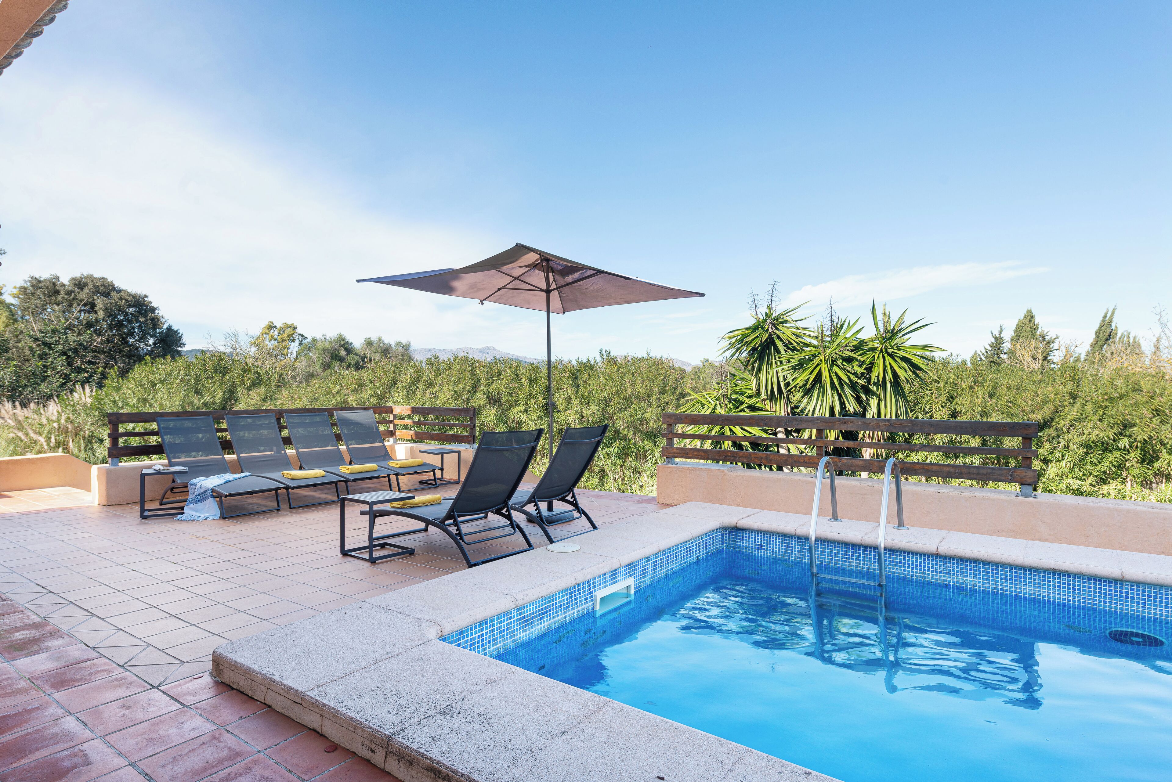 A swimming pool with a tiled edge, surrounded by lounge chairs and a wooden deck.