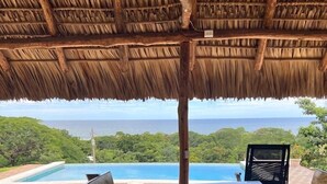 A wooden table with a view of a swimming pool and ocean. - Rancho Agua Fria, Room #2 (Jucuaran)