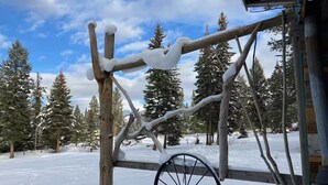 A rustic wooden structure with a large wheel, surrounded by snow-covered trees.