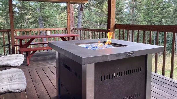 A deck with a metal fire pit, a wooden table, and a bench.