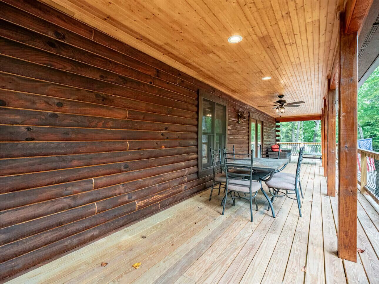 A wooden cabin with a covered porch, a dining table with chairs, and a ceiling fan.