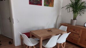 Una zona de menjador amb una taula de fusta i cadires blanques, una planta en test i un moble de bany amb un rellotge.