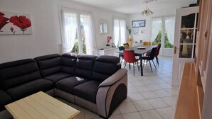 A spacious living room with a sectional sofa, a small coffee table, and a dining area with a table and chairs. - Maison Sainte Cécile near beach and shops, pets welcome (Camiers)
