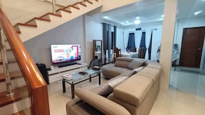 A modern living room with a sofa, coffee table, and a TV. A staircase is visible in the background. - 3 Bedroom Exclusive Gated Home in Manila (Las Piñas)