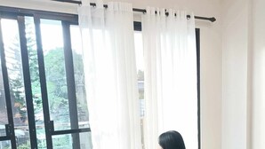 A woman sitting on a beige sofa with a bouquet of red roses beside her, in a room with large windows and sheer curtains. - 3 Bedroom Exclusive Gated Home in Manila (Las Piñas)