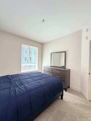 Une chambre à coucher avec un lit, une commode, un miroir et une fenêtre avec des stores.
