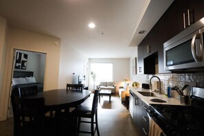 A modern kitchen with dark cabinetry, a stainless steel stove, and a dining area with a round table and chairs. - Wi-Fi • Parking • Fully Furnished 1BR in San Diego (San Diego)
