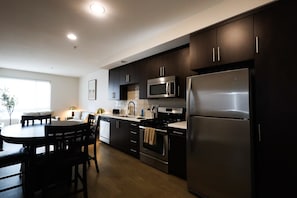 A modern kitchen with dark cabinetry, stainless steel appliances, and a dining area with a round table and chairs.