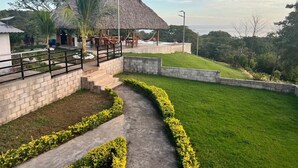 A thatched-roof structure with outdoor seating, surrounded by a landscaped garden and a pathway.