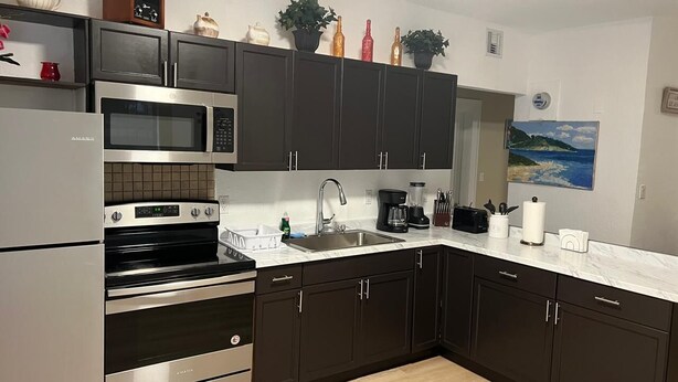 A modern kitchen with dark cabinets, stainless steel appliances, and a white countertop. - Lovely 2-bedroom house with AC in vibrant Miami (Miami)