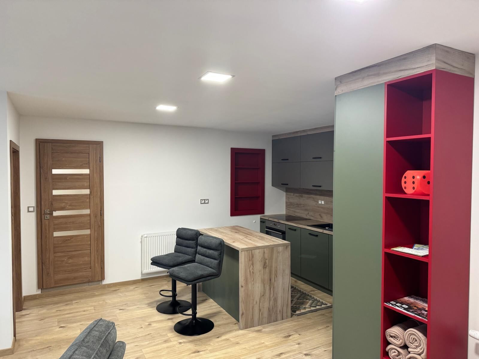 Une cuisine compacte dotée d’un plan de travail en bois, d’une cuisinière encastrée et d’une étagère rouge.