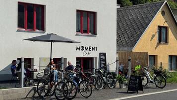 A cafe named 'Moment Cafe' with bicycles parked outside and a signboard for 'PAVA 21Klim NAPOJE'.