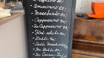 Un tableau noir affiche la carte des boissons, avec les différentes sortes de café et de lait proposés, ainsi que leurs prix.
