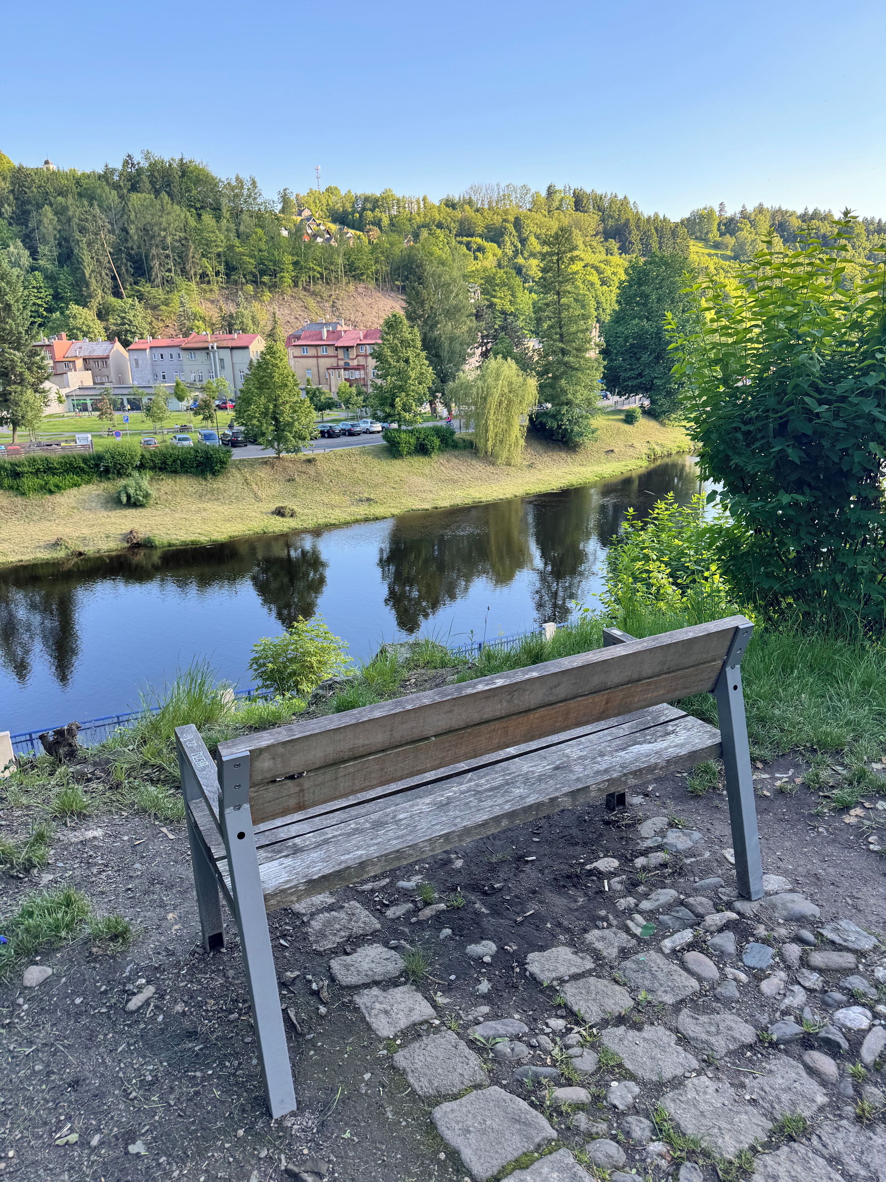 A bench overlooking a calm river with a forested hillside in the background.