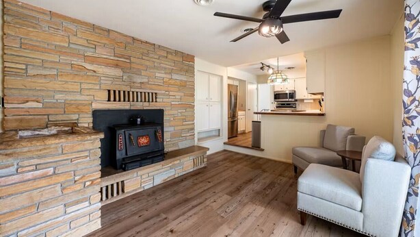 Una sala de estar moderna con chimenea de piedra, ventilador de techo y cocina al fondo.