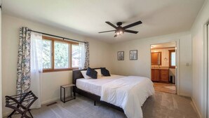 Un dormitorio con cama, ventilador de techo, ventana con cortinas y vista a la cocina.