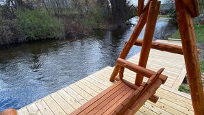 Una terraza de madera con un banco que da a un río.