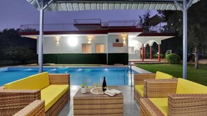 A poolside area with wicker furniture and a covered seating area. - Alaya Stays By Elivaas Luxe Farm Acre - Manesar (Taoru)