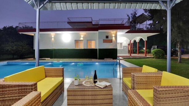 A poolside area with wicker furniture and a covered seating area. - Alaya Stays By Elivaas Luxe Farm Acre - Manesar (Taoru)