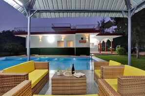 A poolside area with wicker furniture and a covered seating area. - Alaya Stays By Elivaas Luxe Farm Acre - Manesar (Taoru)
