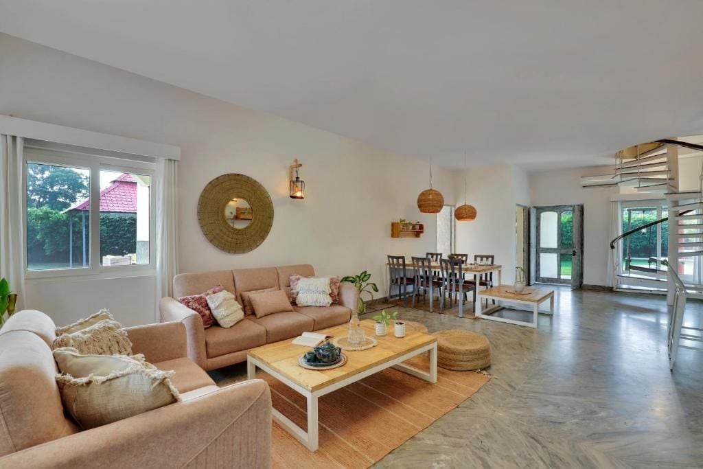 A spacious living area with a sofa, coffee table, and dining table. There is a staircase leading to an upper level.